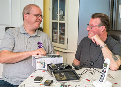 Photo of equipment officer Piers demonstrating some phone equipment to a client at home